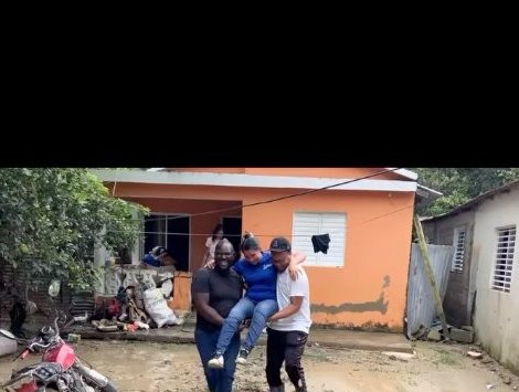 Two Levanta Ministries team members carrying a community member through the mud in front of a home.